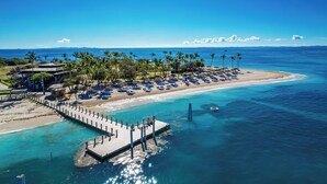 Un resort frente al mar con un muelle, sombrillas de playa y palmeras.