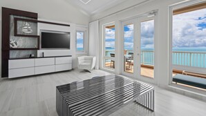 Ein modernes Wohnzimmer mit großem Fernseher, einem weißen Sofa und Meerblick durch bodengroße Fenster.