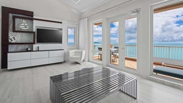 Una sala de estar moderna con un televisor grande, un sofá blanco y vistas al océano a través de amplias ventanas.