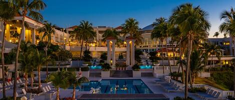 A resort pool area with multiple swimming pools, lounge chairs, and palm trees.