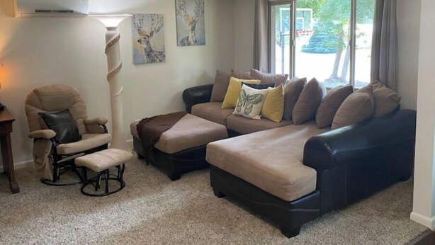 A living room with a sofa, armchair, and ottoman, a fireplace, and artwork on the wall. - Evans Corner-A Libby Original (Libby)