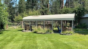 A covered outdoor area with a lawn, a metal fence, and trees in the background. - Evans Corner-A Libby Original (Libby)