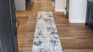 Un pasillo con suelo de madera, un tapete estampado y una zona de cocina con electrodomésticos modernos y una mesa de comedor.