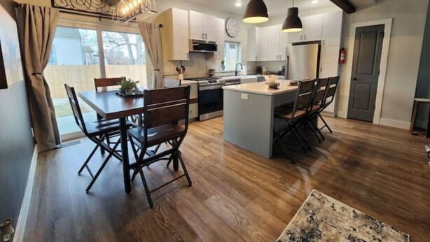 Una cocina amplia con una isla central, suelo de madera, iluminación colgante y vistas al exterior.