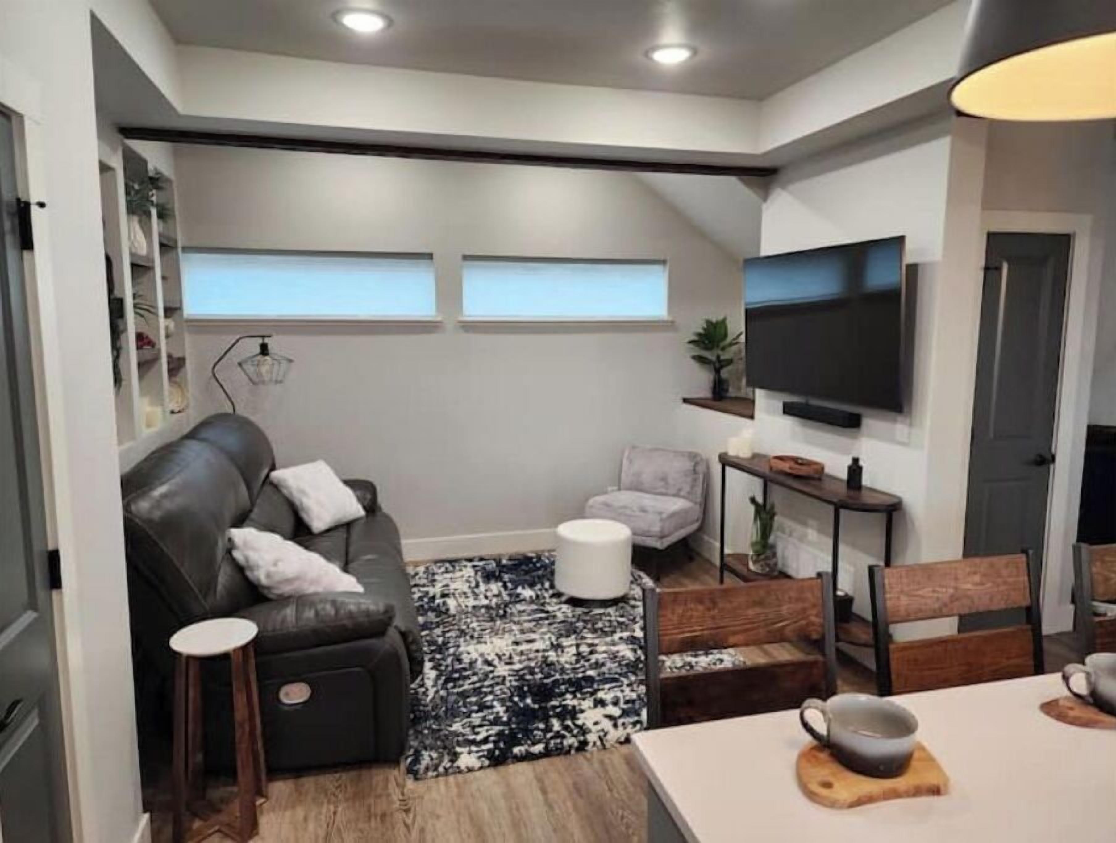 Una sala de estar moderna con un sofá de cuero gris, una mesita redonda pequeña, una mesa de centro y un televisor montado en la pared.