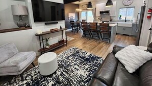 Una sala de estar moderna con un sofá, un televisor y un comedor con sillas y una mesa.