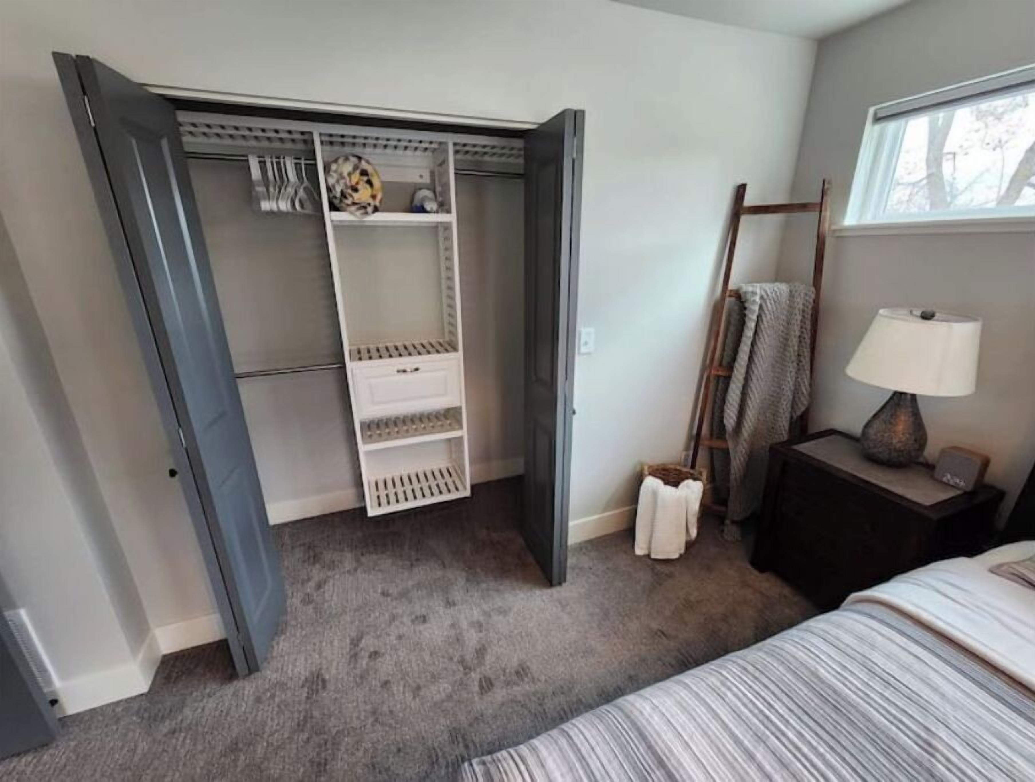 Une chambre à coucher avec un lit, une table de chevet avec une lampe, une armoire et une fenêtre donnant sur des arbres.