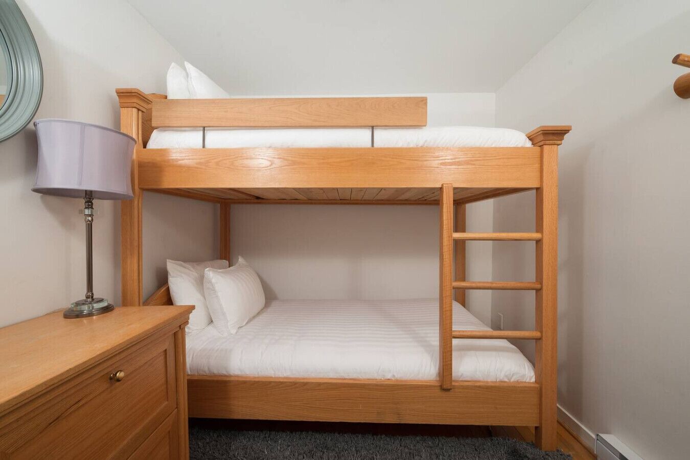 Kerrossänky, jossa on puinen runko, yöpöytä lampun kanssa ja pieni laatikko.