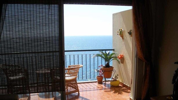 Uma varanda com vista para o mar, mobiliário de vime e plantas em vasos.
