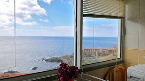 A room with a large window overlooking the sea, a red vase on a table, and a washing machine. - Magos Sunrise - Apt with sea view (Santa Cruz)