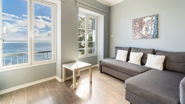 A living room with a grey sofa, a small white table, and large windows overlooking the sea. - Barreirinha II Near Old Town With Nice Ocean Views (Funchal)