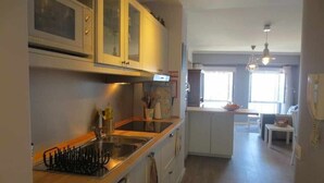 Una cocina con horno integrado, microondas y lavaplatos. Hay una zona de comedor con mesa y sillas.