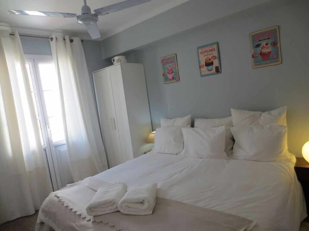 Un lit bien fait, avec du linge de lit et des serviettes blancs, un ventilateur de plafond et une armoire.