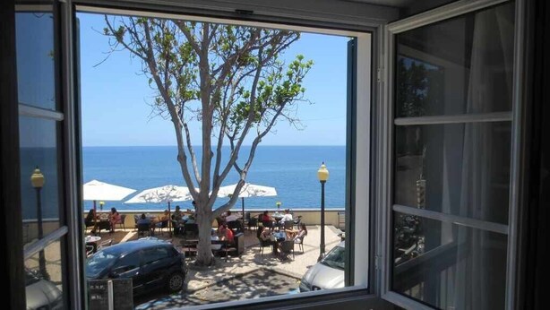Vista desde una ventana sobre una playa con sombrillas y gente.