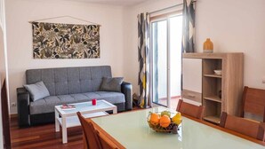 A living room with a grey sofa, a white coffee table, and a dining table with chairs. There is a fruit bowl on the dining table. - Rosalina's Apartment (Caniço)