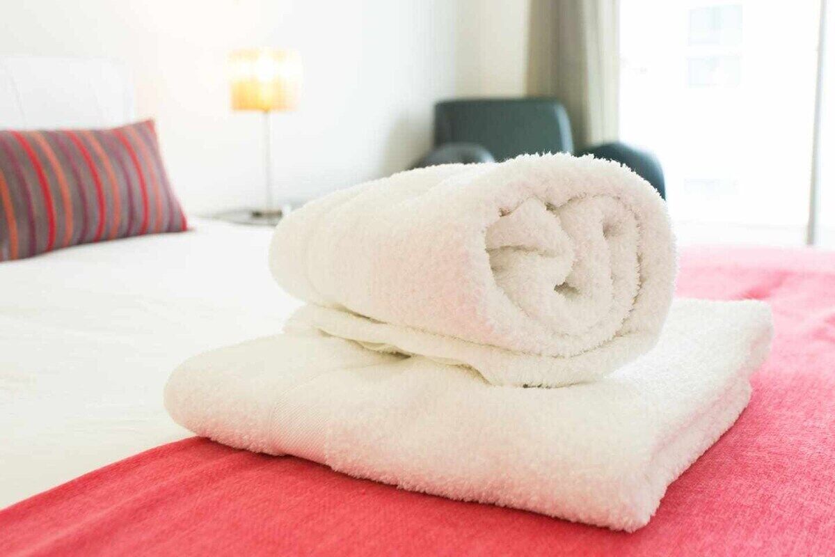 Een netjes gevouwen witte handdoek op een rode sprei in een hotelkamer.