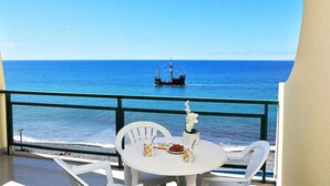 Ein Balkon mit Tisch und Stühlen, der auf ein ruhiges Meer mit einem Schiff in der Ferne blickt.