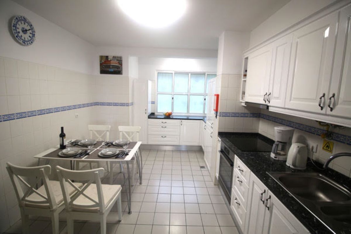 Une cuisine avec des meubles blancs, un plan de travail noir et un sol carrelé.