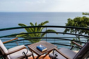 Uma varanda com vista para o mar, uma mesa com um livro e duas cadeiras.