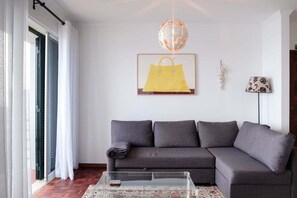 Una sala de estar con un sofá gris, una mesa de centro de vidrio, un tapiz estampado, una lámpara globo, un bolso amarillo enmarcado y una lámpara.