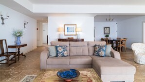 A spacious living room with a beige sectional sofa, a coffee table, and a dining area with wooden furniture. - Vila da Falésia-With Pool and views (Caniço)
