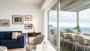 A modern living room with a blue sofa, a floral armchair, and a dining area with a view of the ocean. - Vila da Falésia-With Pool and views (Caniço)
