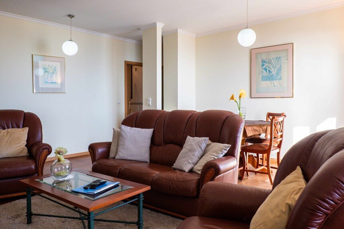 A living room with a brown leather sofa set, a glass coffee table, and a dining area with a wooden table and chairs.