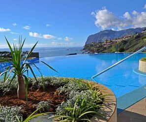 En klar, blå pool uden kant med udsigt over havet og bjergene.