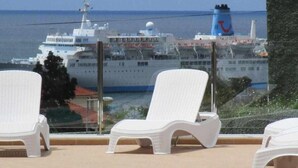 Een zwembadgedeelte met witte ligbedden en een cruiseschip in de verte.