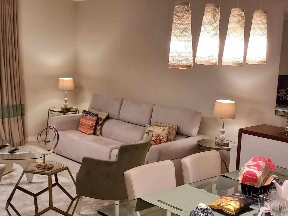 A modern living room with a sofa, armchairs, a glass coffee table, and a side table with a lamp.