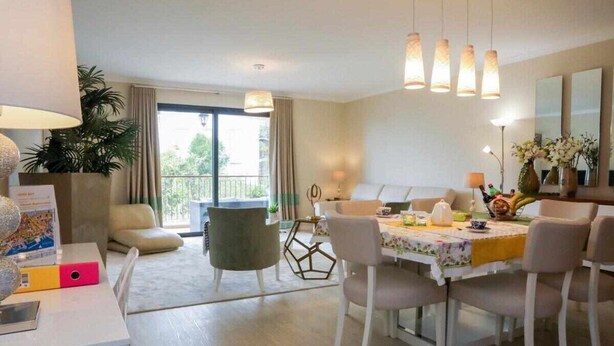 Een moderne eethoek met een tafel voor vier personen, omringd door stoelen. Er is een groot raam met gordijnen, een potplant en uitzicht op het omliggende landschap.