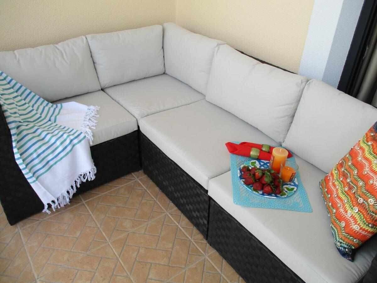 A corner sofa with a striped blanket, a tray with fruits and candles, and a colorful pillow.