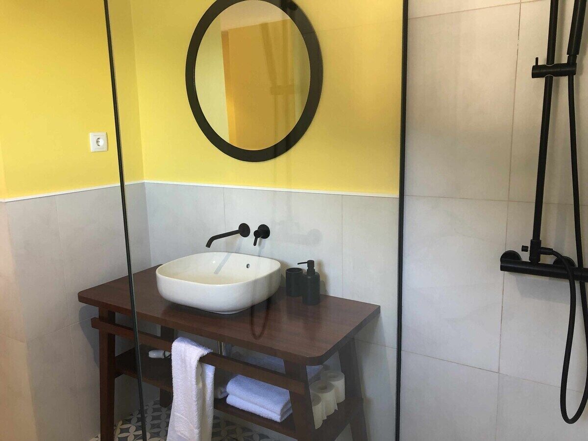 Une salle de bain avec un lavabo blanc, un robinet noir et un miroir rond placé sur un meuble-lavabo en bois.