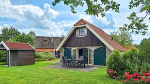 A two-story house with a sloped roof, a front porch with a table and chairs, and a small shed in the yard. - 3 bedroom gorgeous home in IJhorst (IJhorst)
