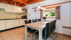 A kitchen with white cabinets, a wooden table, and black chairs. There is a window with curtains and a clock on the wall. - 3 bedroom gorgeous home in IJhorst (IJhorst)