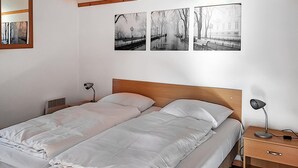 A double bed with white bedding, a wooden headboard, a bedside table with a lamp, and a nightstand with a lamp. There are three black and white photographs on the wall. - 3 bedroom gorgeous home in IJhorst (IJhorst)