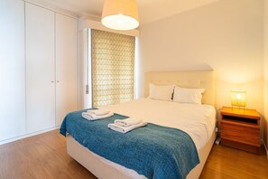 A bedroom with a bed, a nightstand, a wardrobe, and a patterned curtain.