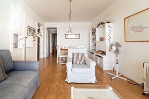 A modern living room with a grey sofa, a white armchair, a dining table, and a bookshelf.