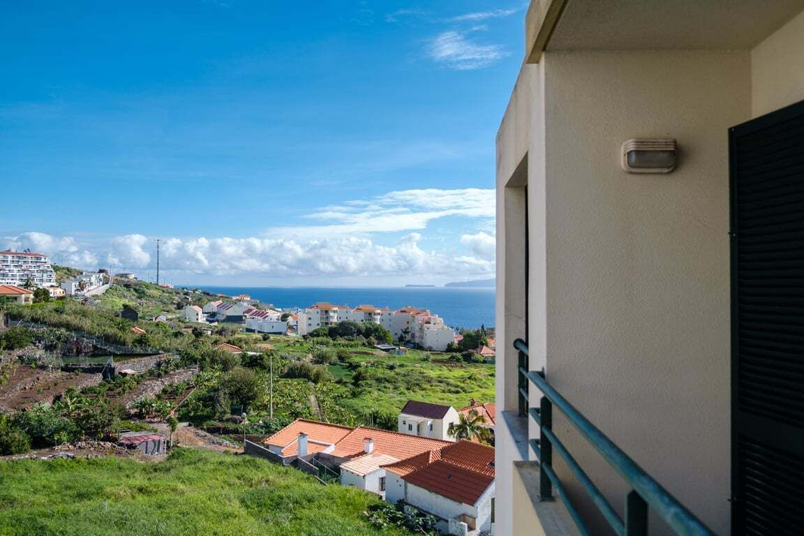 Een balkon met uitzicht op een kustplaatsje, gebouwen en de zee.