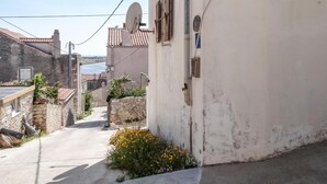 A narrow street with a white building on the right, a stone wall on the left, and a view of the sea in the distance.