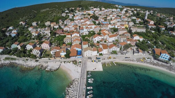 An aerial view of a coastal town with houses, a pier, and boats.