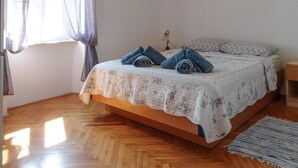 A bedroom with a wooden bed, a patterned bedspread, and a window with sheer curtains.