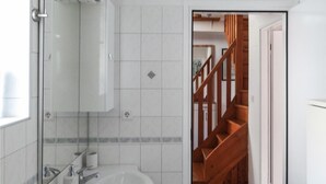 A bathroom with a white sink, mirror, and a wooden staircase leading to another room.