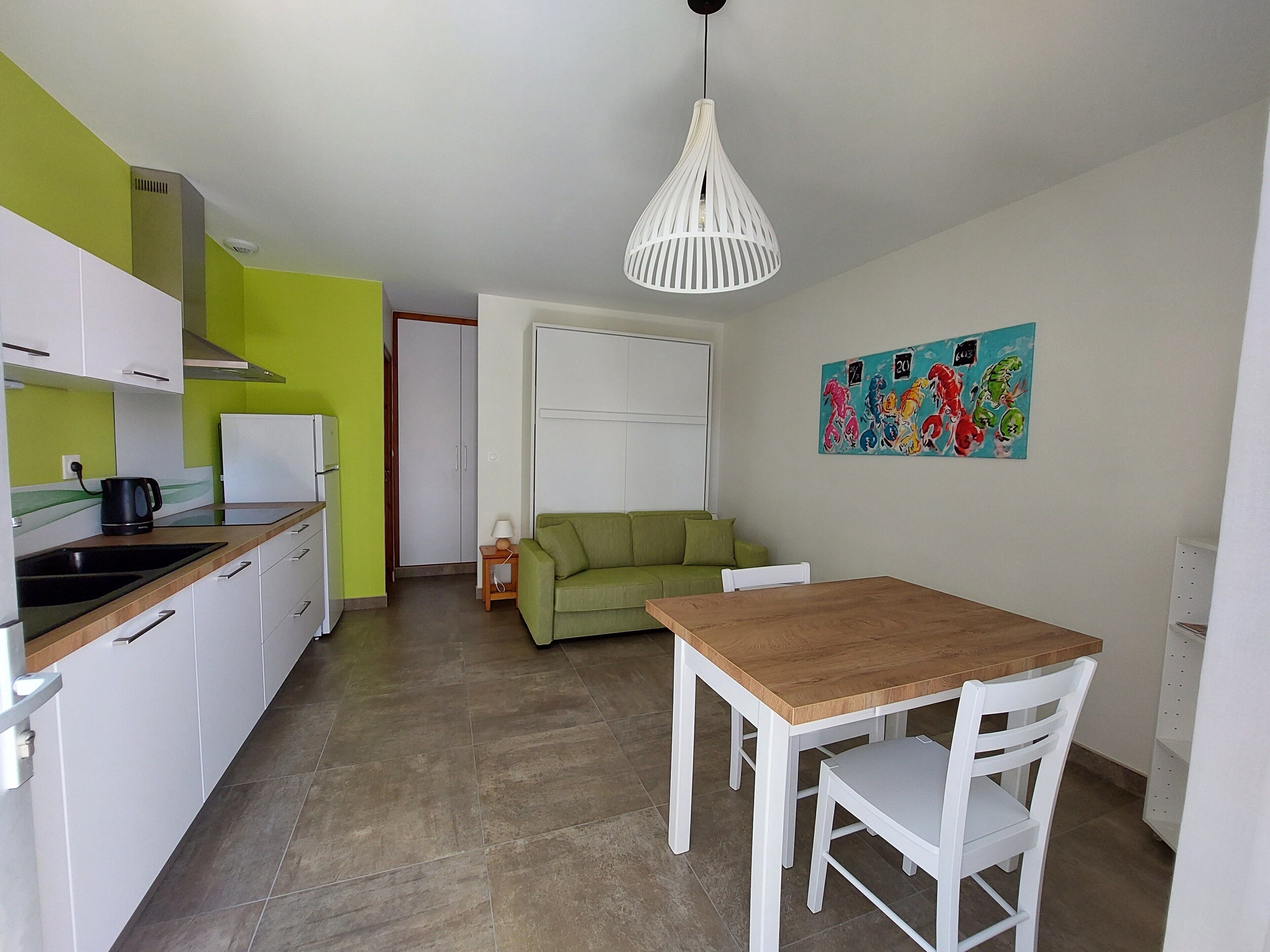 A compact kitchen with white cabinets, a green wall, and a white ceiling light.