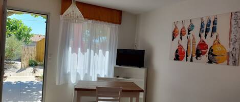 A modern living room with a wooden dining table, a white TV stand, and a painting on the wall.