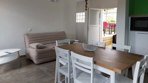 Un espace de vie compact comprenant un canapé, une table à manger avec des chaises, un petit coin cuisine avec un four à micro-ondes et une porte donnant sur un patio extérieur.