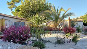 Un jardin doté d’une terrasse en bois, de différentes plantes et d’un bâtiment dont le toit est recouvert de tuiles.