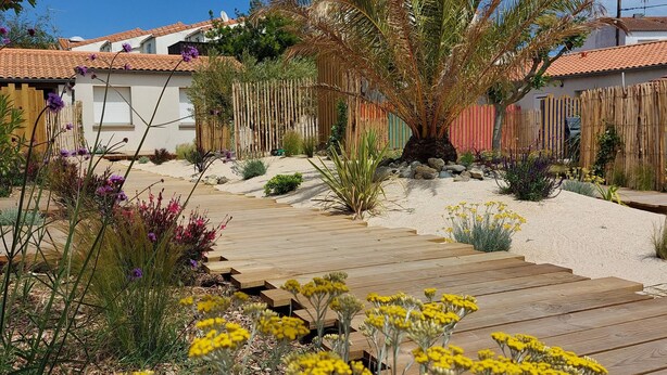 Un jardin avec une terrasse en bois, diverses plantes et un palmier.