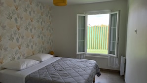Une chambre à coucher avec un lit, une fenêtre donnant sur un paysage dégagé, une lampe jaune et un radiateur.
