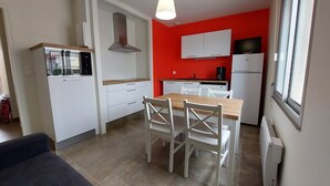 A compact kitchen with white cabinets, a dining table with chairs, and a red accent wall.